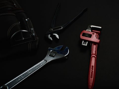 A shifter, a pipe wrench and pliers on a dark bench